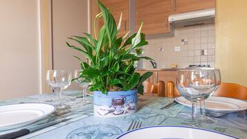 Et spisebord dækket med tallerkener, bestik og vinglas, med en potteplante i midten.