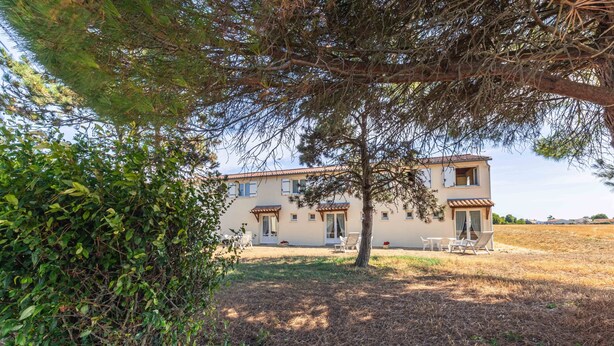 A two-story building with a patio area, surrounded by trees and shrubs. - Duplex No. 2345 – 40m² – Seaside Residence (Port-des-Barques)