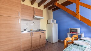 A kitchen with wooden cabinets, a white refrigerator, a microwave, and a dining table with chairs. - Duplex No. 2345 – 40m² – Seaside Residence (Port-des-Barques)