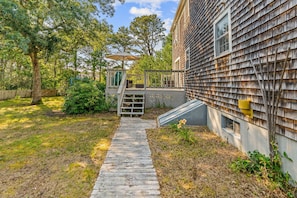 A wooden deck leading to a house with a covered outdoor seating area. - Mashpee Gem with a Private Yard, Volleyball, BBQ and a Fire pit! (Mashpee)