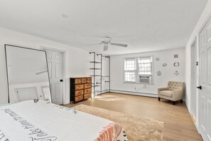 Een slaapkamer met een bed, een dressoir, een kledingroede, een stoel en een plafondventilator.
