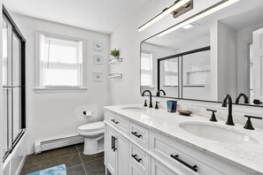 Een moderne badkamer met een wit wastafelmeubel, twee wasbakken, een grote spiegel en een raam met zonwering.