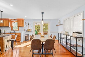 Een moderne keuken met houten kastjes, een eethoek met een tafel en stoelen, en uitzicht op het landschap door een glazen deur.