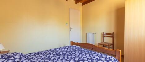 Un dormitorio con techo de madera, una cama con colcha estampada, una silla y un radiador.