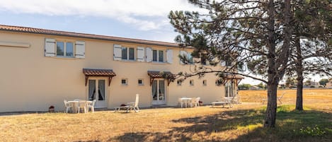 Un bâtiment à deux étages, doté d’un toit plat, de nombreuses fenêtres et d’un patio aménagé avec du mobilier d’extérieur.