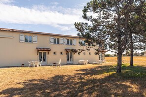 Ein zweistöckiges Gebäude mit flachem Dach, zahlreichen Fenstern und einer Terrasse mit Gartenmöbeln.