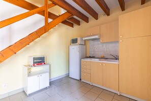 A compact kitchen with a built-in microwave, a white refrigerator, and wooden cabinets. - Duplex No. 1 – 70m² – Seaside Residence (Port-des-Barques)