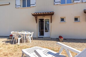 An outdoor seating area with a table and chairs, a covered patio, and a building entrance. - Duplex No. 1 – 70m² – Seaside Residence (Port-des-Barques)
