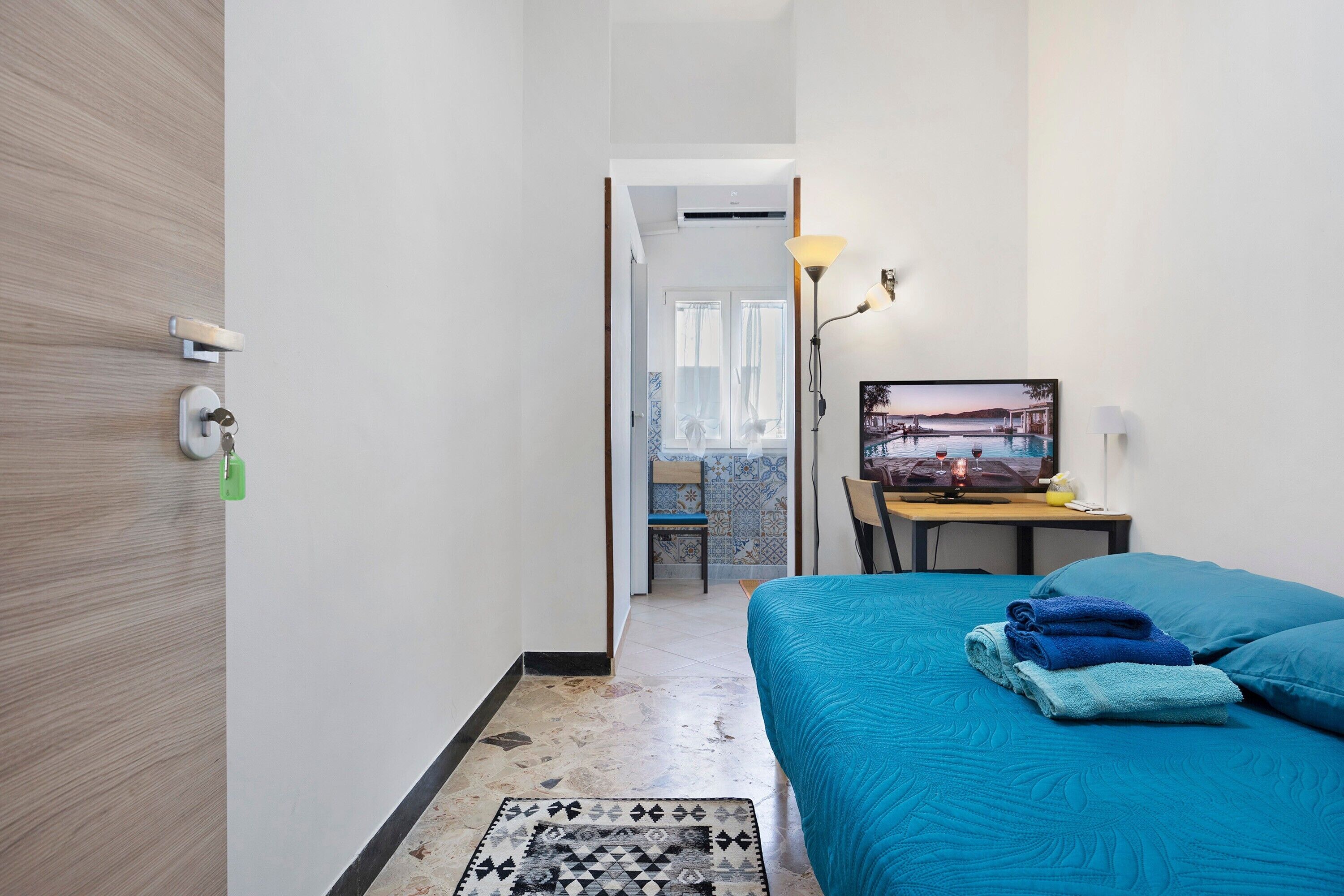 A hotel room with a bed, a desk with a computer, a TV, and a view of a pool.