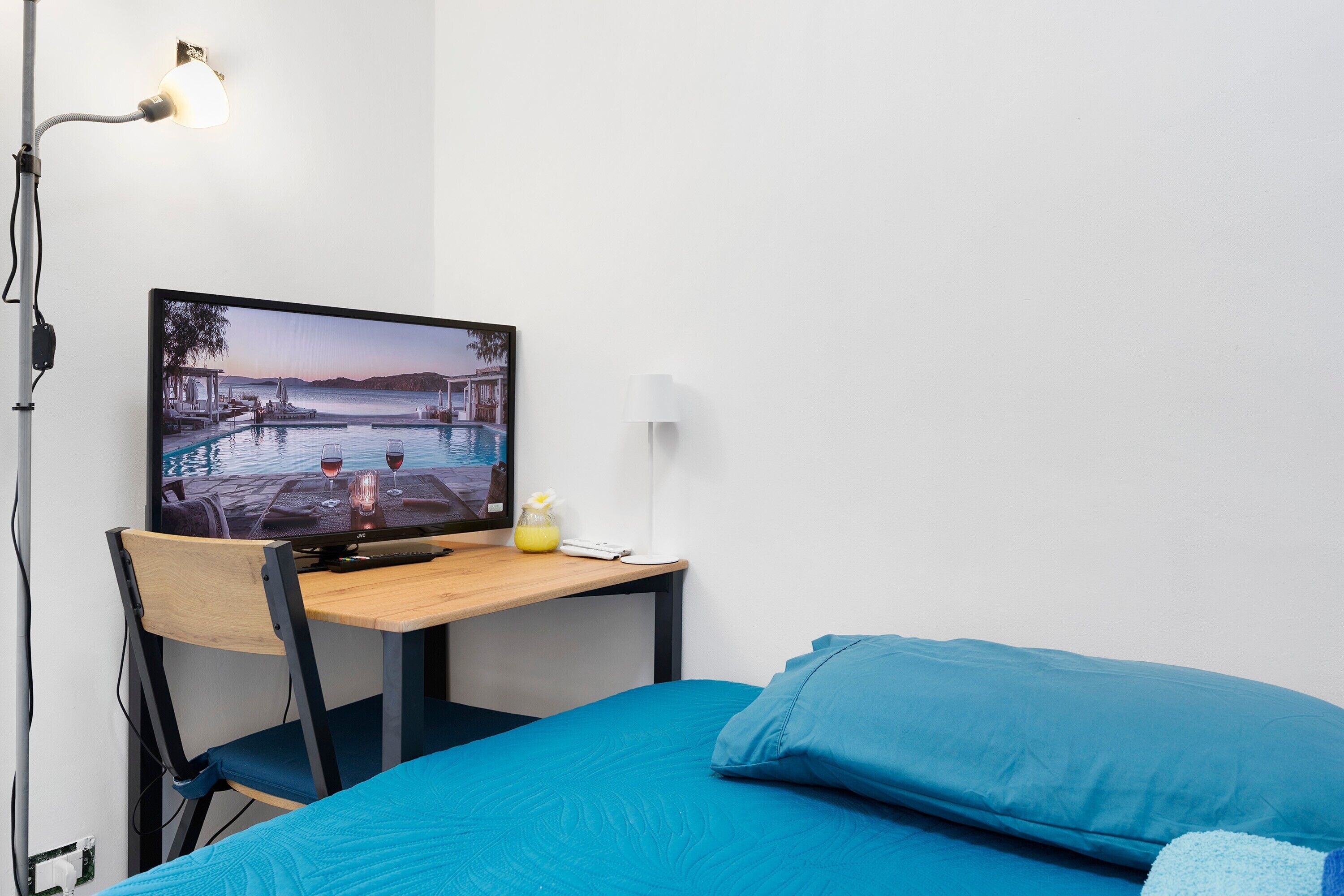 Habitación de hotel con cama, escritorio con televisor que muestra una vista panorámica, una silla y una lámpara.