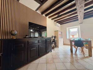 Une cuisine avec des meubles de couleur sombre, un mur recouvert de lambris en bois et un coin repas comprenant une table et des chaises.
