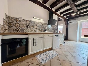 Une cuisine avec des carreaux décoratifs, un four encastré, des meubles blancs et une poutre en bois au plafond.