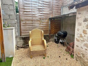 Une chaise en osier dans un jardin, avec un barbecue et un mur en pierre.