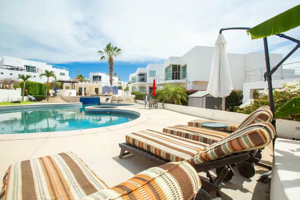 A pool area with lounge chairs, a pool, and modern buildings in the background.