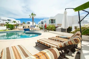 A pool area with lounge chairs, a pool, and modern buildings in the background. - Large 4-bedroom home-2 Pools - Arch View Rooftop (Cabo San Lucas)
