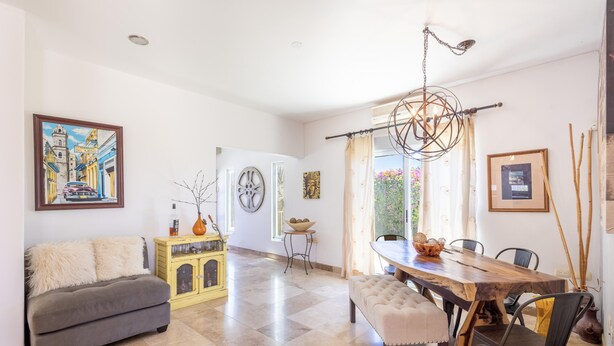 A dining area with a wooden table, chairs, a chandelier, and a painting on the wall. - Large 5-bedroom home-2 Pools - Arch View Rooftop (Cabo San Lucas)