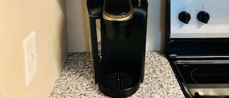Una cocina con cafetera, microondas y estante con dos tazas blancas y dos jarras de vidrio.