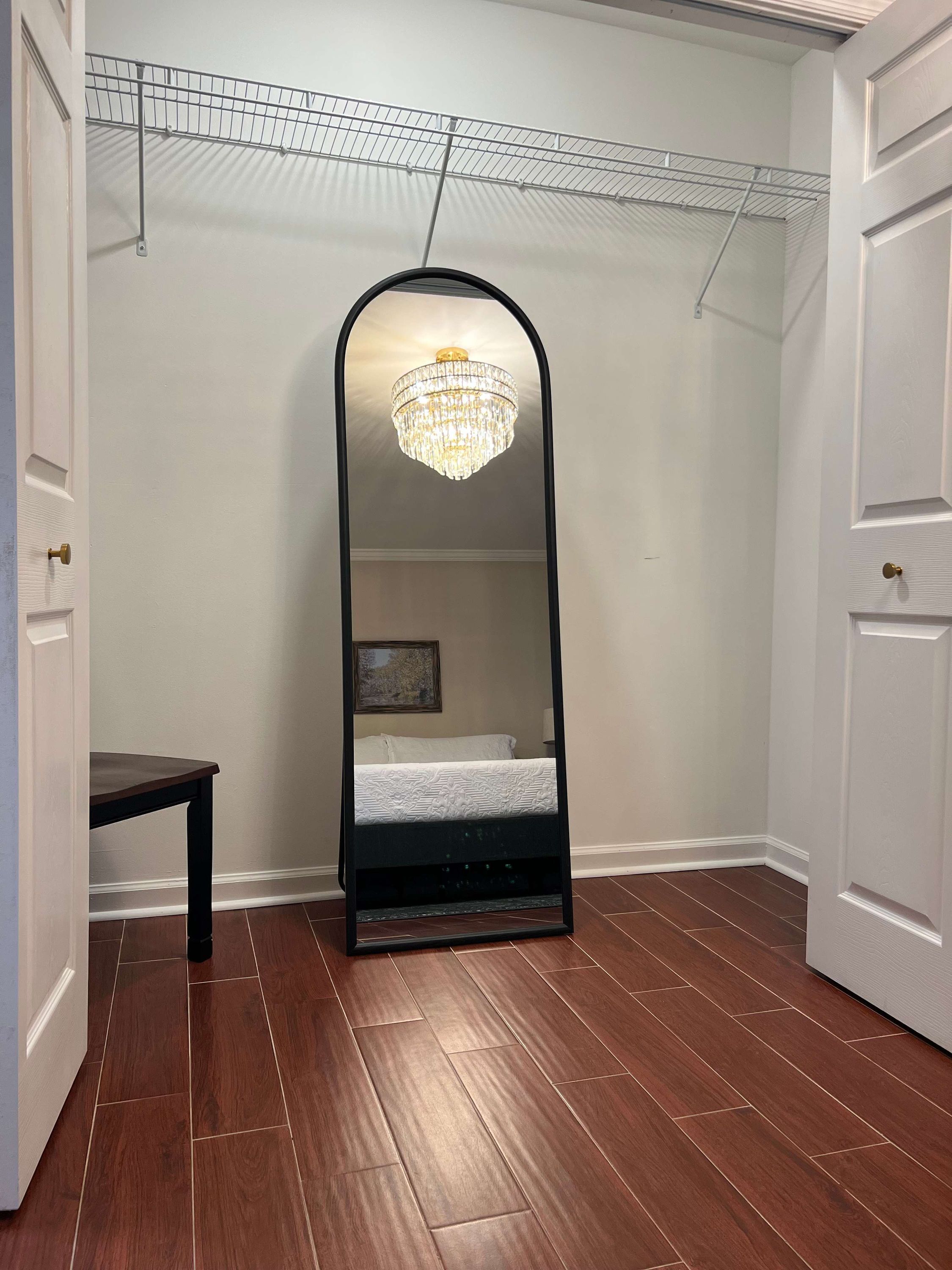 Een kamer met een grote spiegel, een bed, een houten vloer en een plafondlamp.