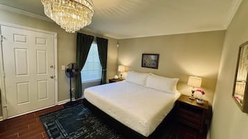 A bedroom with a large bed, a chandelier, a fan, and a nightstand with a lamp.