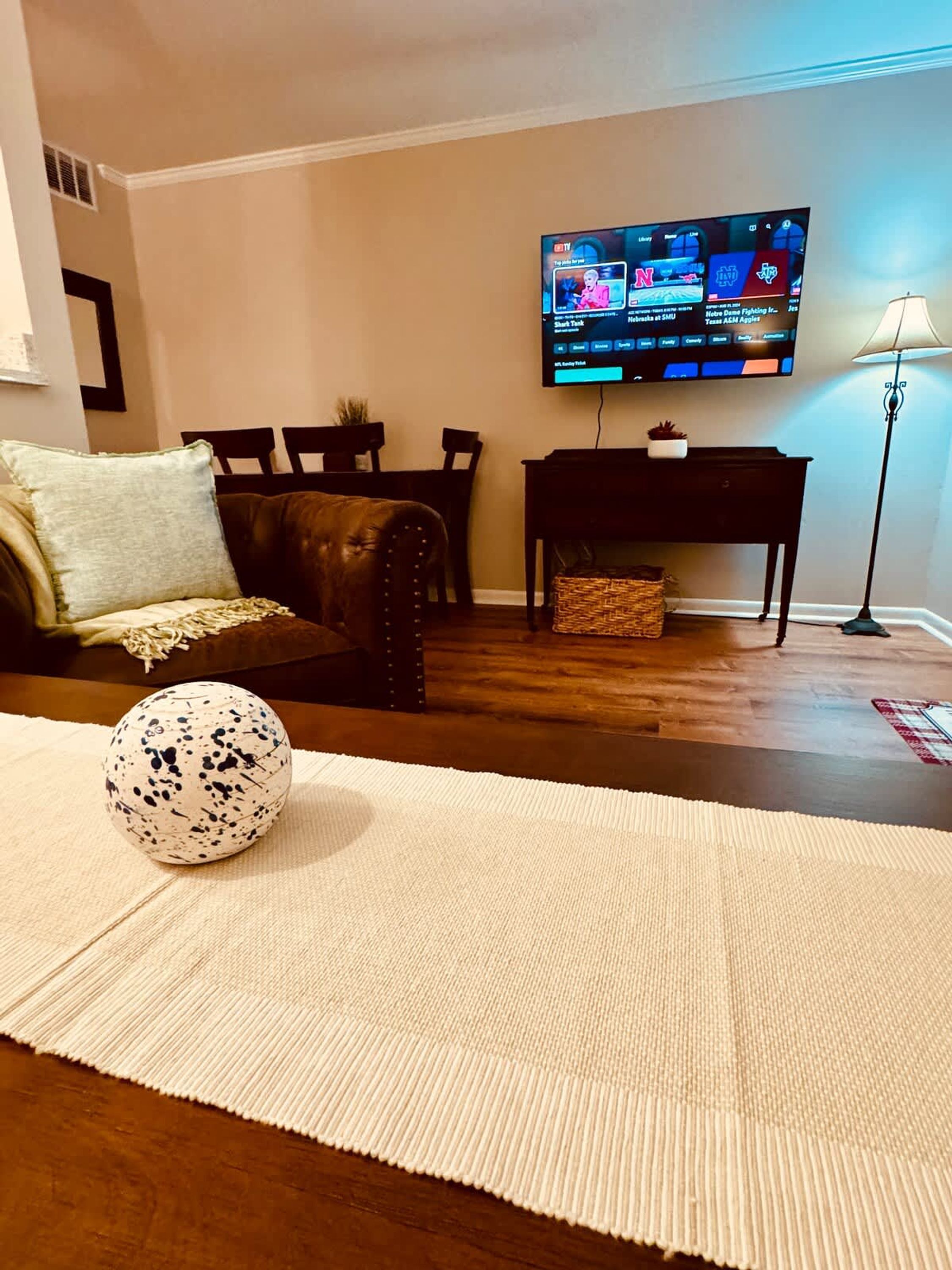 A living room with a sofa, a coffee table with a decorative item, a TV mounted on the wall, and a lamp.