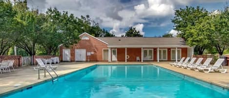 Una piscina rectangular con un edificio de ladrillo al fondo, rodeada de árboles.