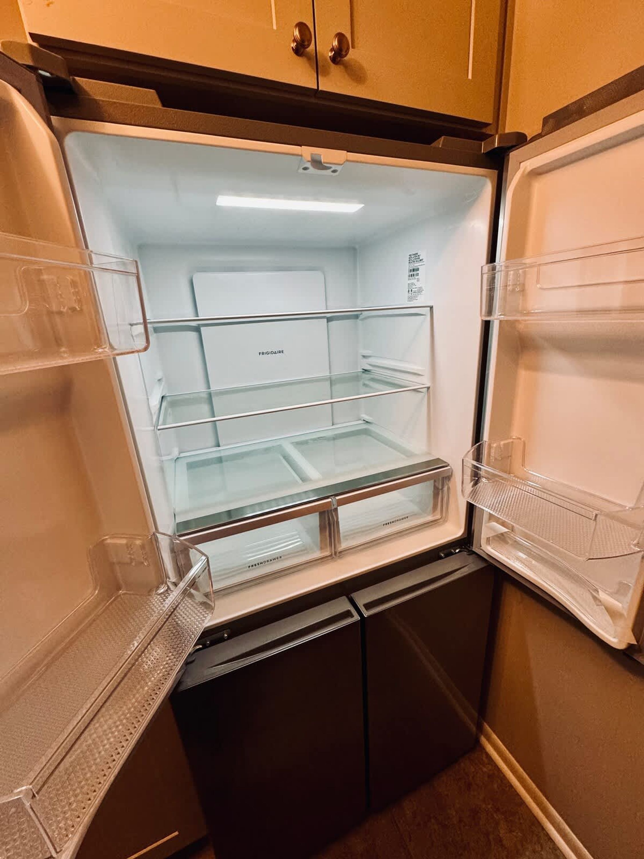 An open refrigerator with clear shelves and a freezer compartment, no visible contents, and a small built-in ice maker.