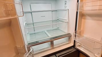 An open refrigerator with clear shelves and a freezer compartment, no visible contents, and a small built-in ice maker.