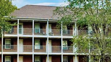 A multi-story building with a brick facade, multiple balconies, and a grassy area in front.