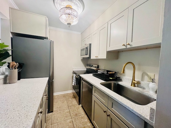 A kitchen with a stainless steel refrigerator, a microwave, a dishwasher, a sink with a gold faucet, and a chandelier.