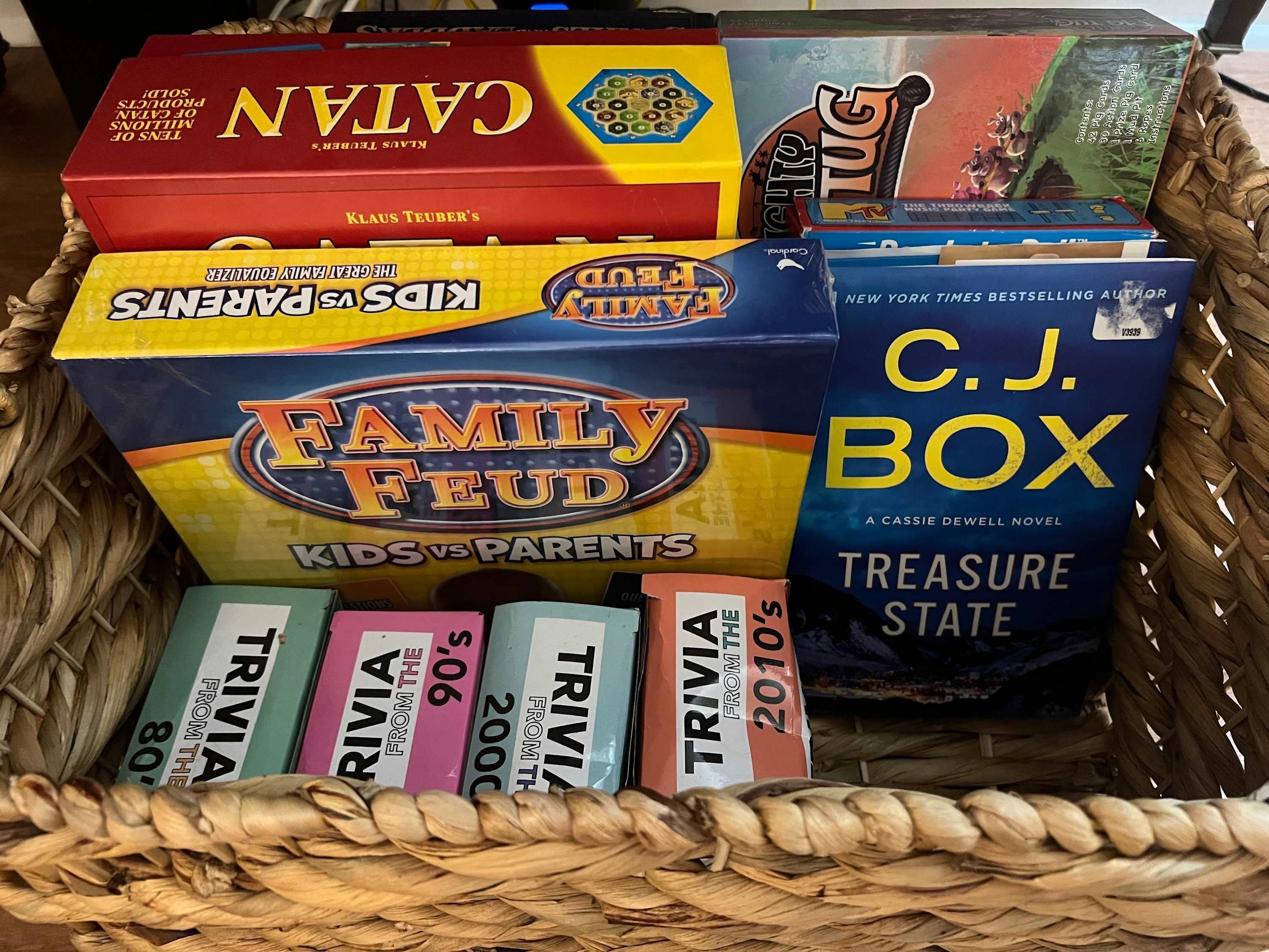 A collection of board games and trivia books in a woven basket.