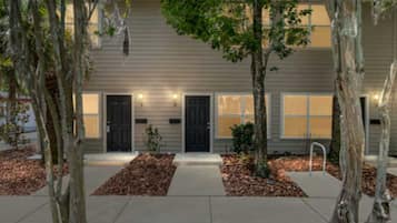 A two-story building with a symmetrical facade, a central entrance, and a small front yard with trees and mulch.
