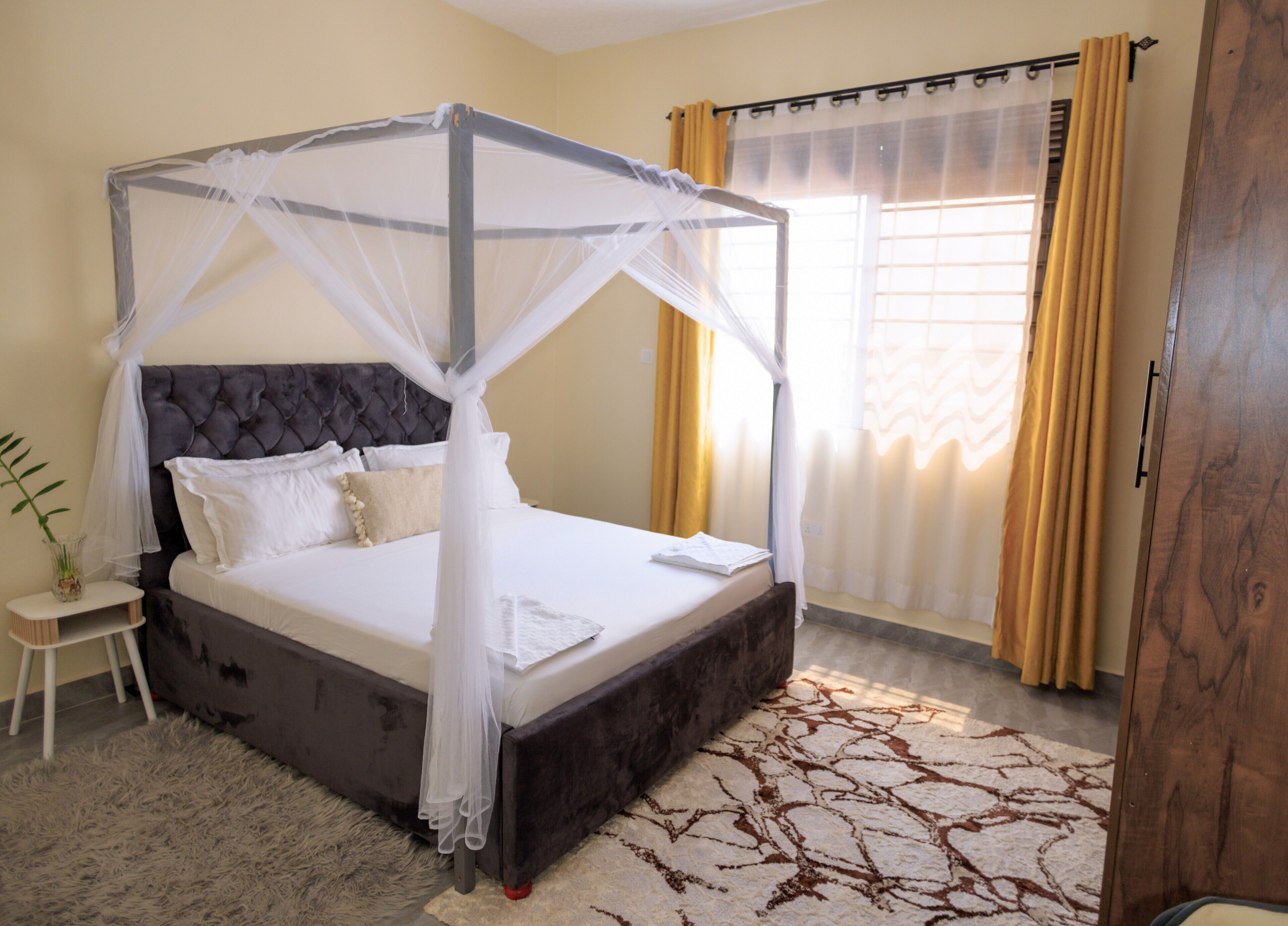 Ein Himmelbett mit Baldachin, ein Nachttisch mit einer Vase und ein gemustertes Teppich.