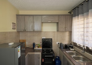 A compact kitchen with a gas stove, a built-in oven, a sink, and cabinets. - Our Beautiful Home,2 Bedrooms. Close to shops, amenities & Ndere Cultural Centre (Kisasi)