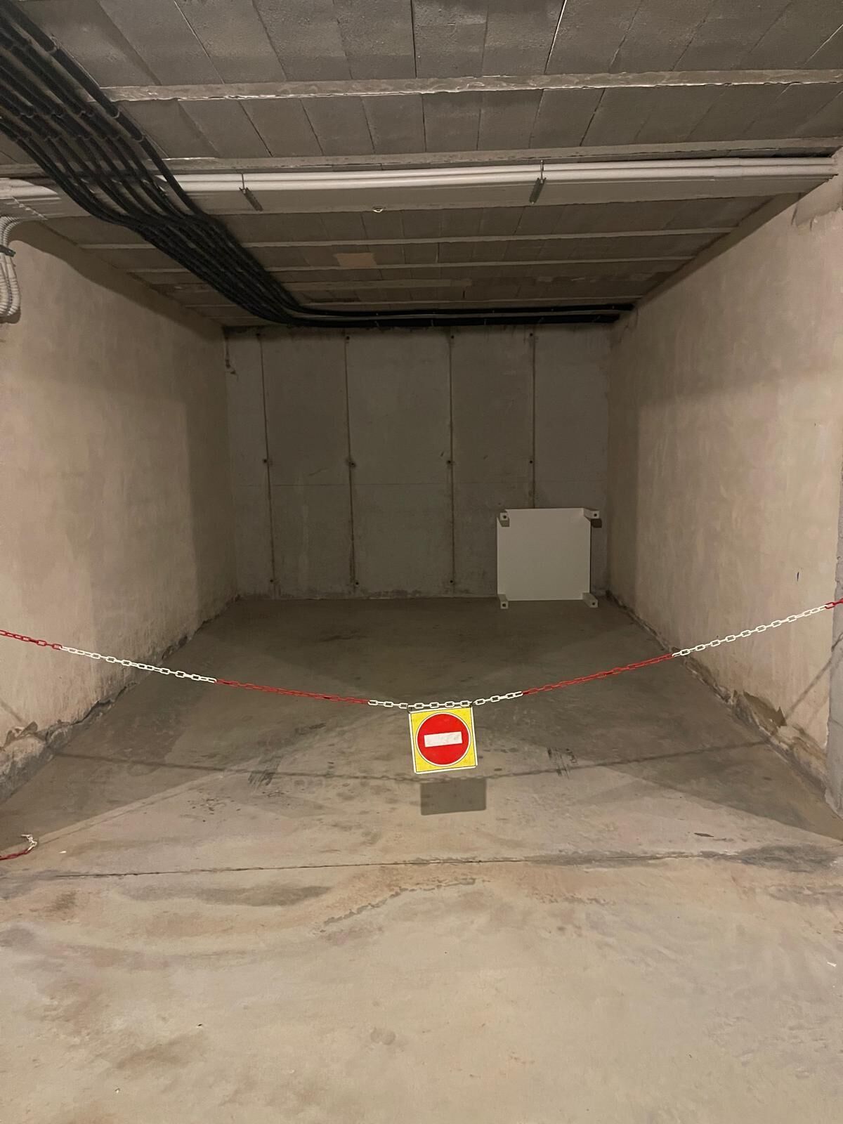 A vacant room with a 'no entry' sign, concrete walls, and a chain barrier.