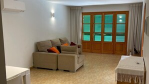 Ein Wohnzimmer mit einer Couch, einem kleinen Tisch, einem Holzschrank und einem Fenster mit Jalousien.