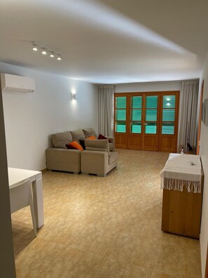 Ein Wohnzimmer mit einer Couch, einem kleinen Tisch, einem Holzschrank und einem Fenster mit Jalousien.