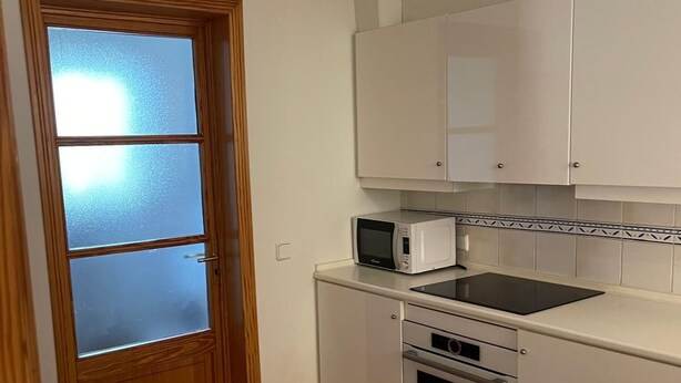 Eine kleine Küche mit Mikrowelle, Backofen und weißen Schränken.