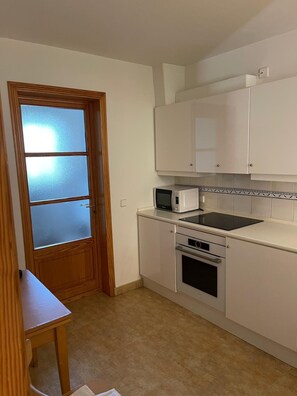 A compact kitchen with a microwave, oven, and white cabinets. - Sa Ràpita Beach, ocean views, 2 bedrooms, pool, and parking. Balcon des Trenc (Sa Ràpita)