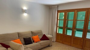 Ein Wohnzimmer mit einem beigen Sofa, einem kleinen Sessel und einer Holztür mit grünen Fensterläden.