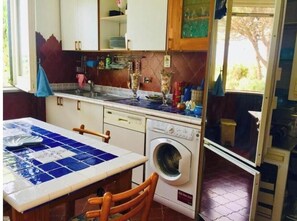A compact kitchen with a washing machine, a tiled backsplash, and a window with a view. - Spacious apartment in a villa with a fully equipped garden and a rooftop with a panoramic view (Procida)