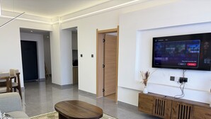 Ein modernes Wohnzimmer mit einem an der Wand befestigten Flachbildfernseher, einem Holztisch und einer Couch mit gemusterten Kissen.