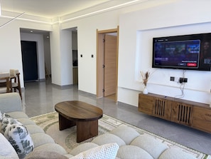 A modern living room with a flat-screen TV mounted on the wall, a wooden coffee table, and a sofa with patterned cushions. - Serene 2-bedroom apartment perfect for your Nairobi getaway (Nairobi)