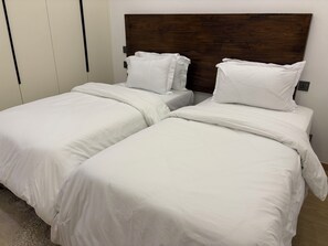 Ein Schlafzimmer mit zwei Betten, jeweils mit weißer Bettwäsche und Kissen, einem Holzkopfstück und einem weißen Kleiderschrank.
