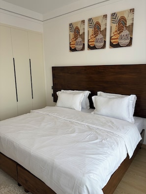 A bedroom with a large bed, a wooden headboard, a wardrobe, and three wall-mounted paintings. - Serene 2-bedroom apartment perfect for your Nairobi getaway (Nairobi)