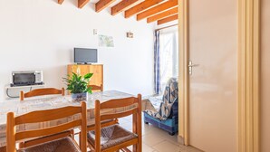 Uma sala de jantar com uma mesa de madeira, cadeiras, uma televisão pequena e um vaso de planta.