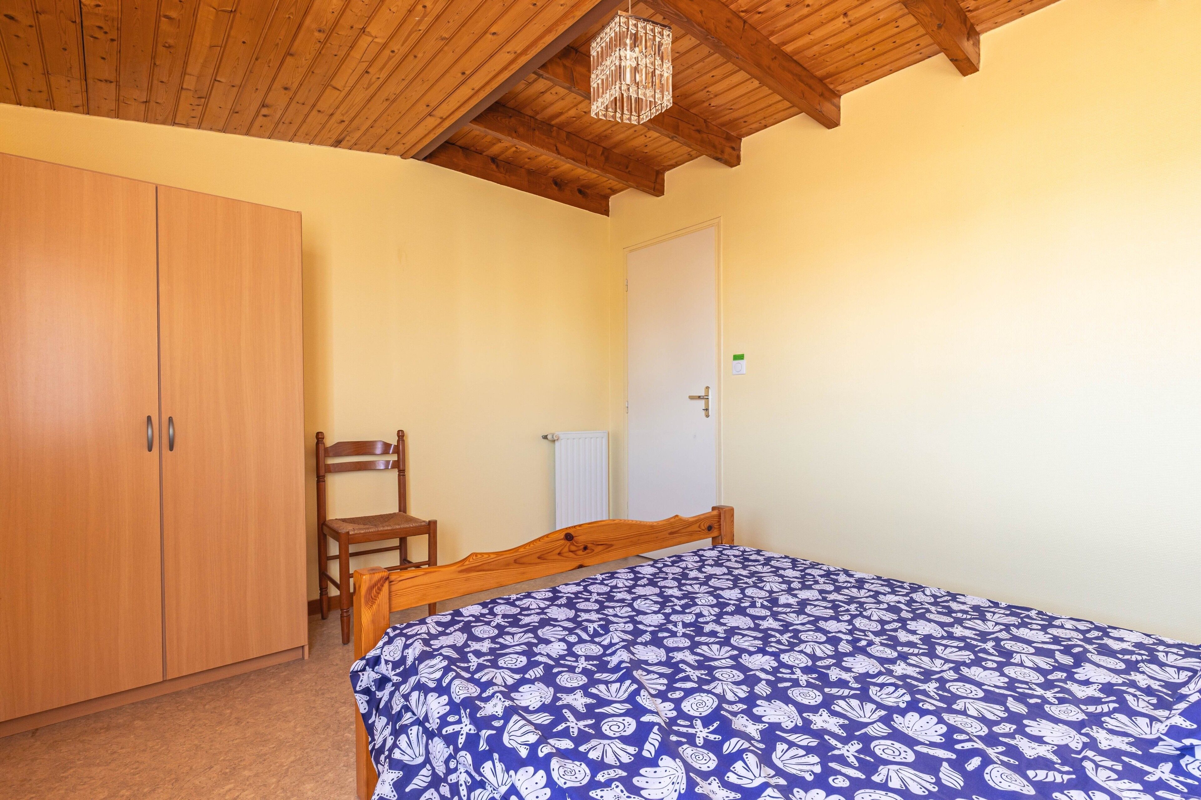 A bedroom with a wooden wardrobe, a wooden bed frame, a chair, and a radiator.
