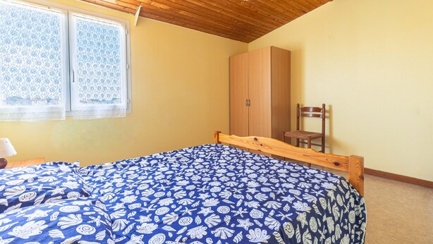 Quarto com teto de madeira, cama com colcha azul estampada, guarda-roupa e uma cadeira.