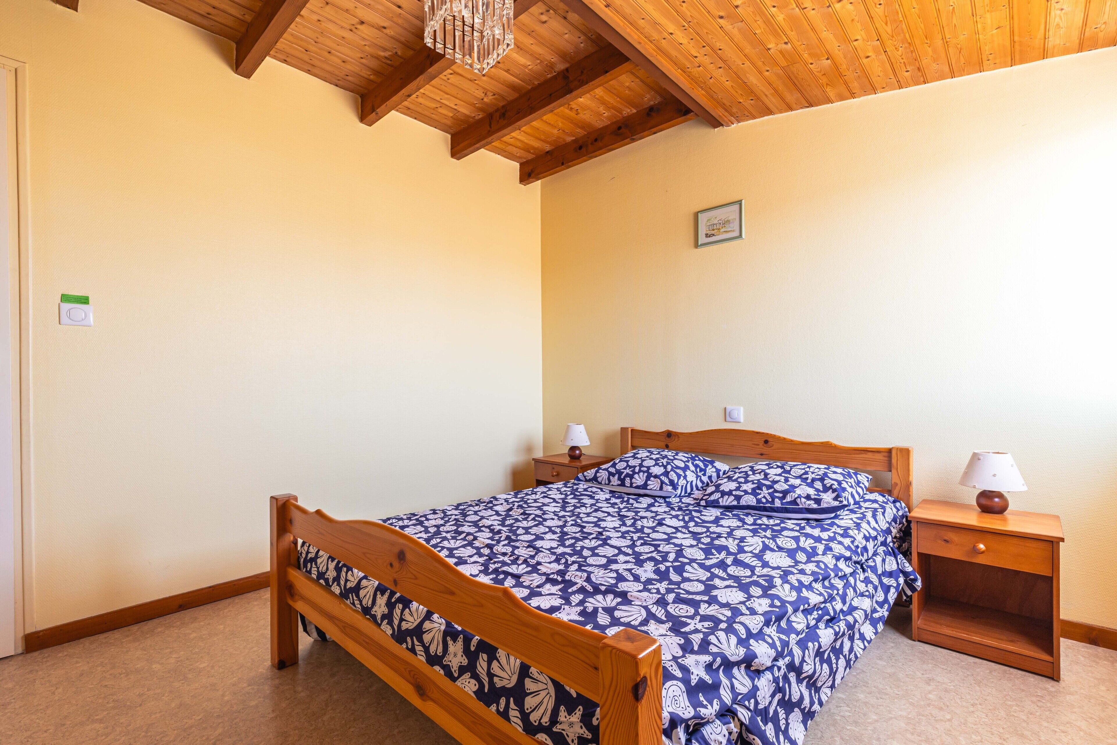 Um quarto com uma cama de madeira, duas mesas de cabeceira, um criado-mudo, uma luminária na parede e um ventilador de teto.