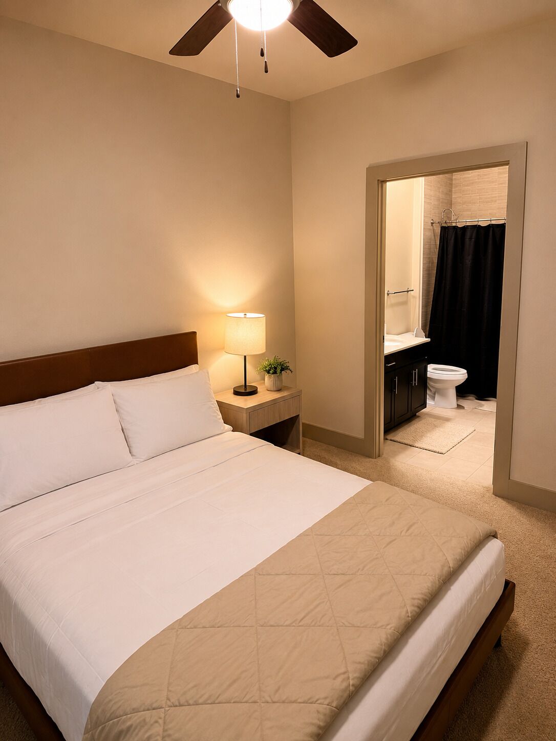 A hotel room with a bed, bedside lamp, nightstand, and a view of the bathroom.