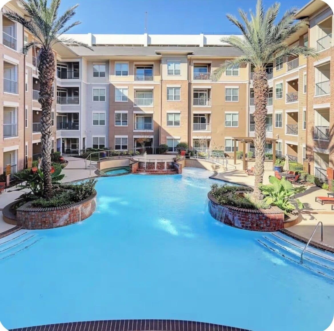 A multi-story hotel with a central pool surrounded by palm trees and a small waterfall feature.